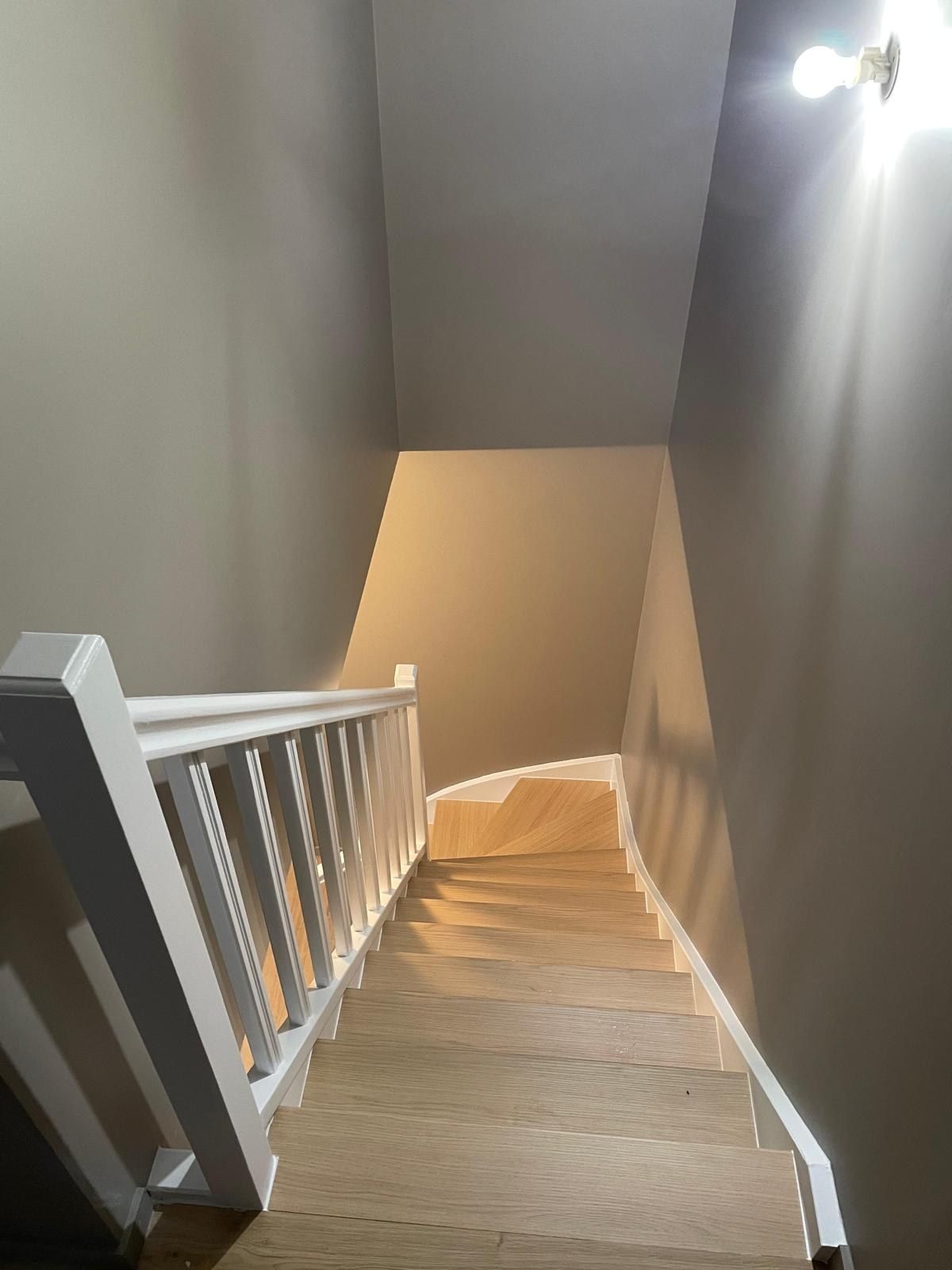 Cage d’escalier repeinte en gris avec rampe et garde-corps blancs, marches en bois