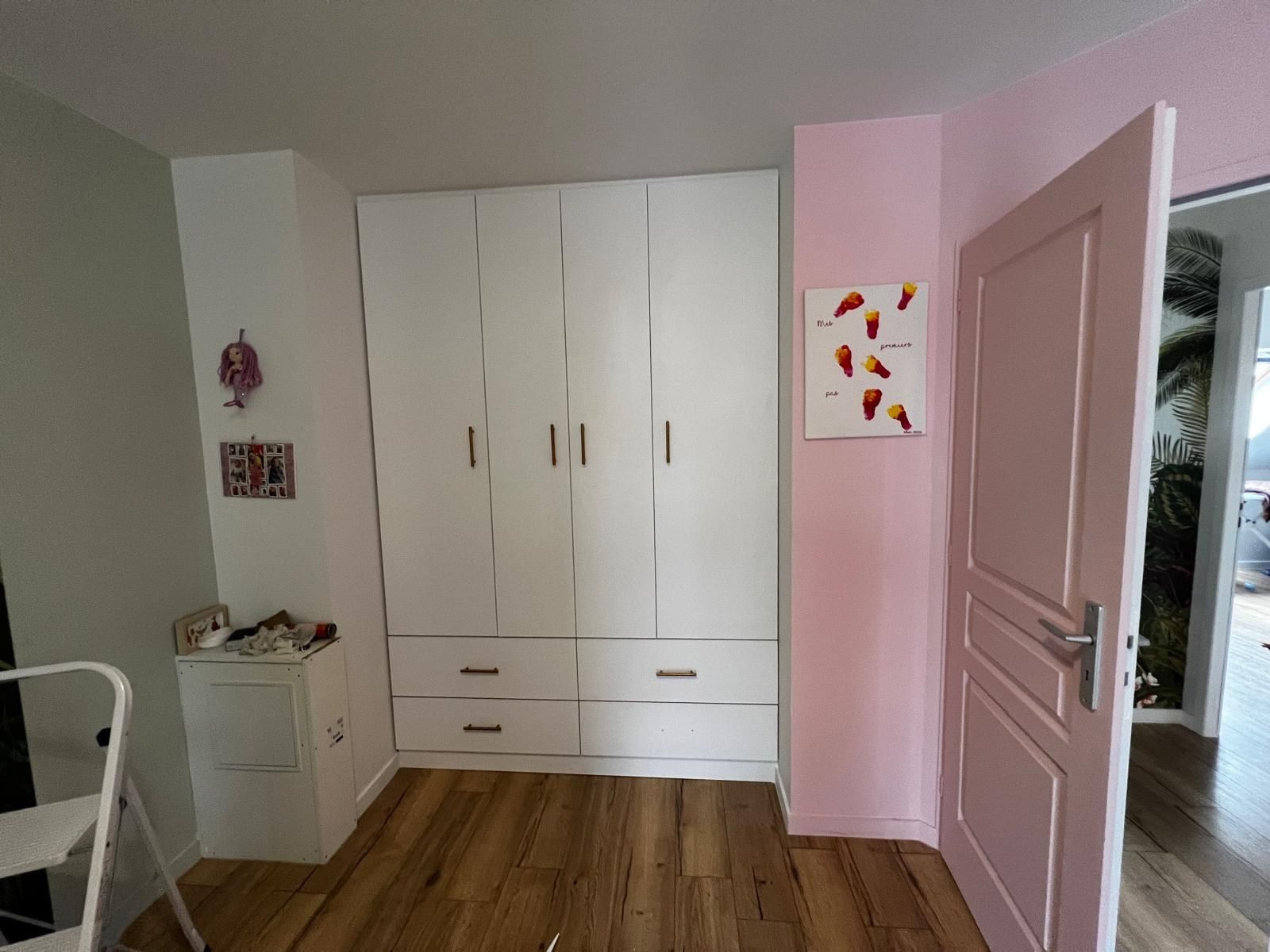 Chambre avec des placards blancs toute hauteur, un mur et une porte peints en rose poudré
