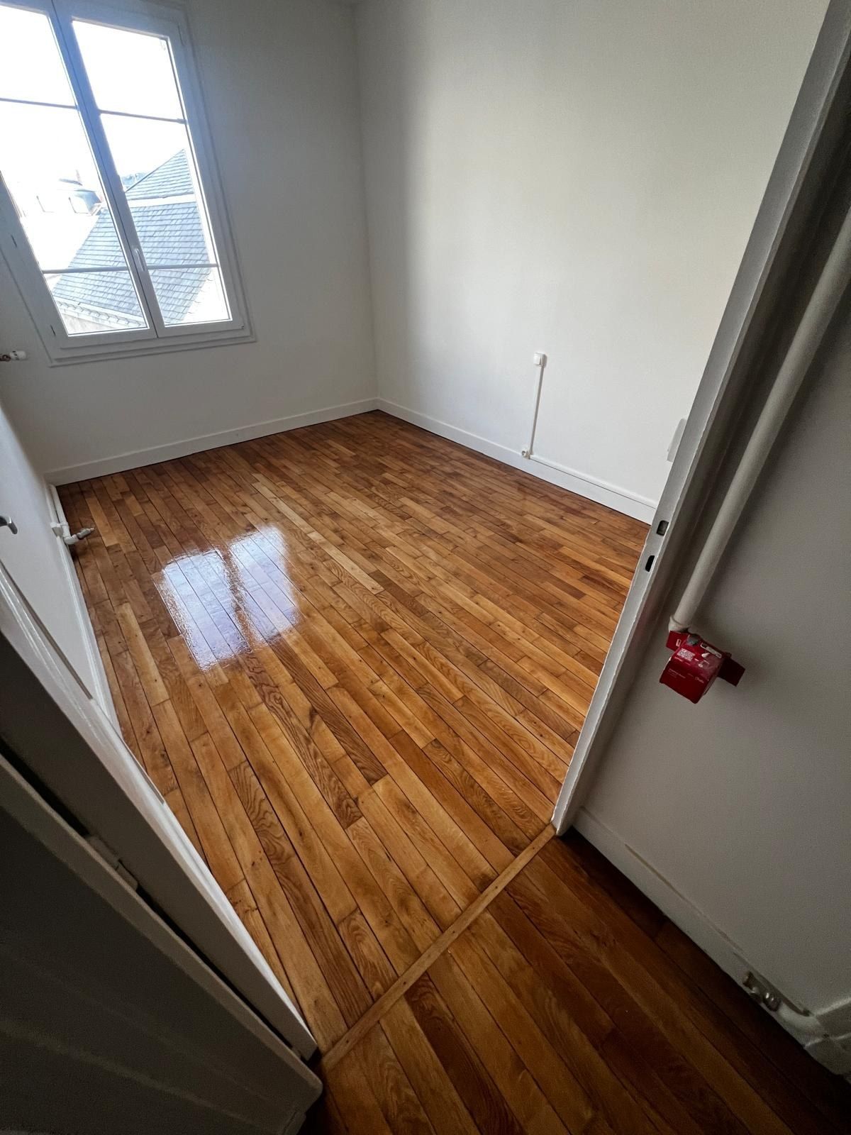 Palier au parquet verni brillant, murs blancs et fenêtre à petits bois