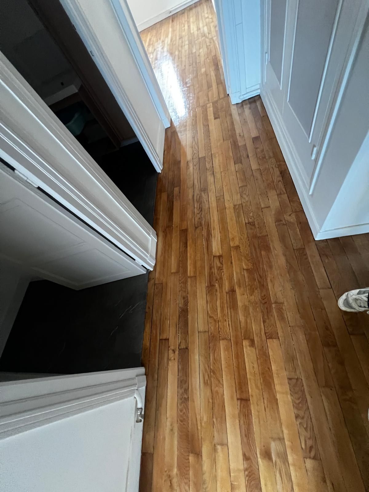 Couloir au parquet en bois clair vu en plongée, entre des portes blanches