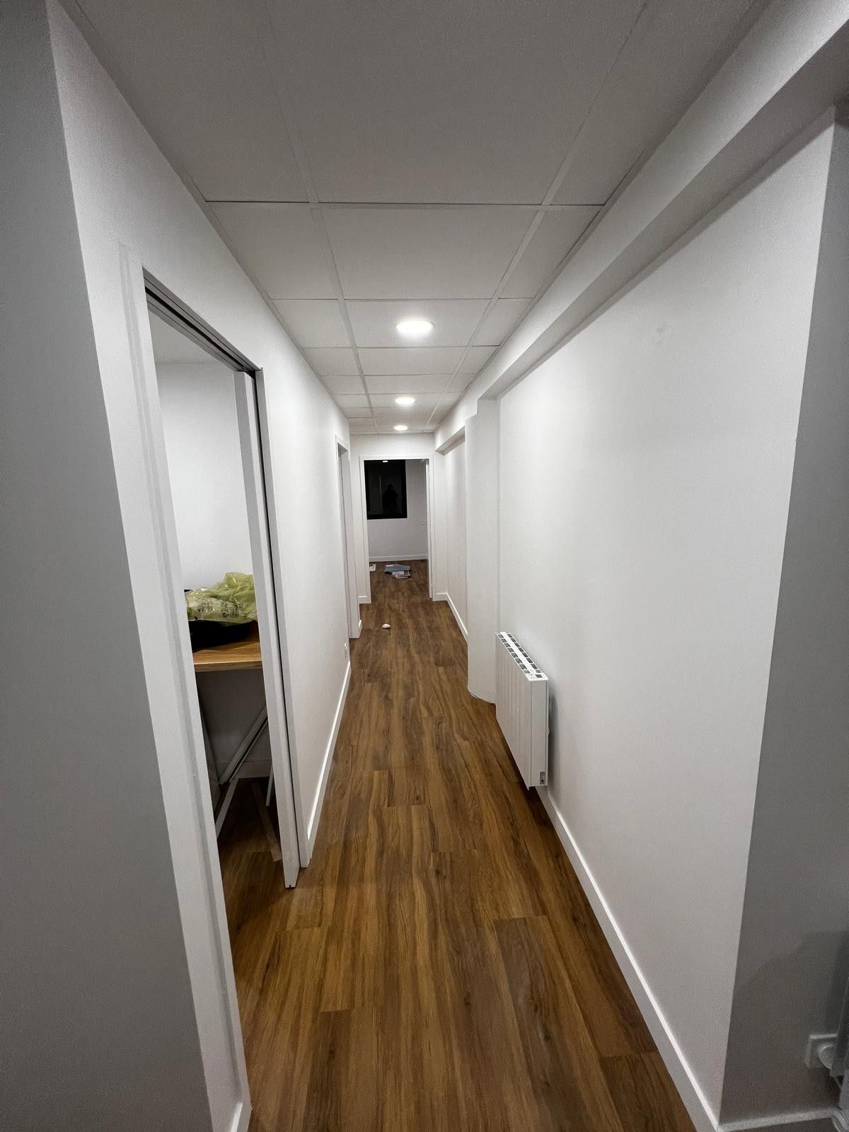Couloir rénové avec sol aspect bois, murs blancs et spots encastrés