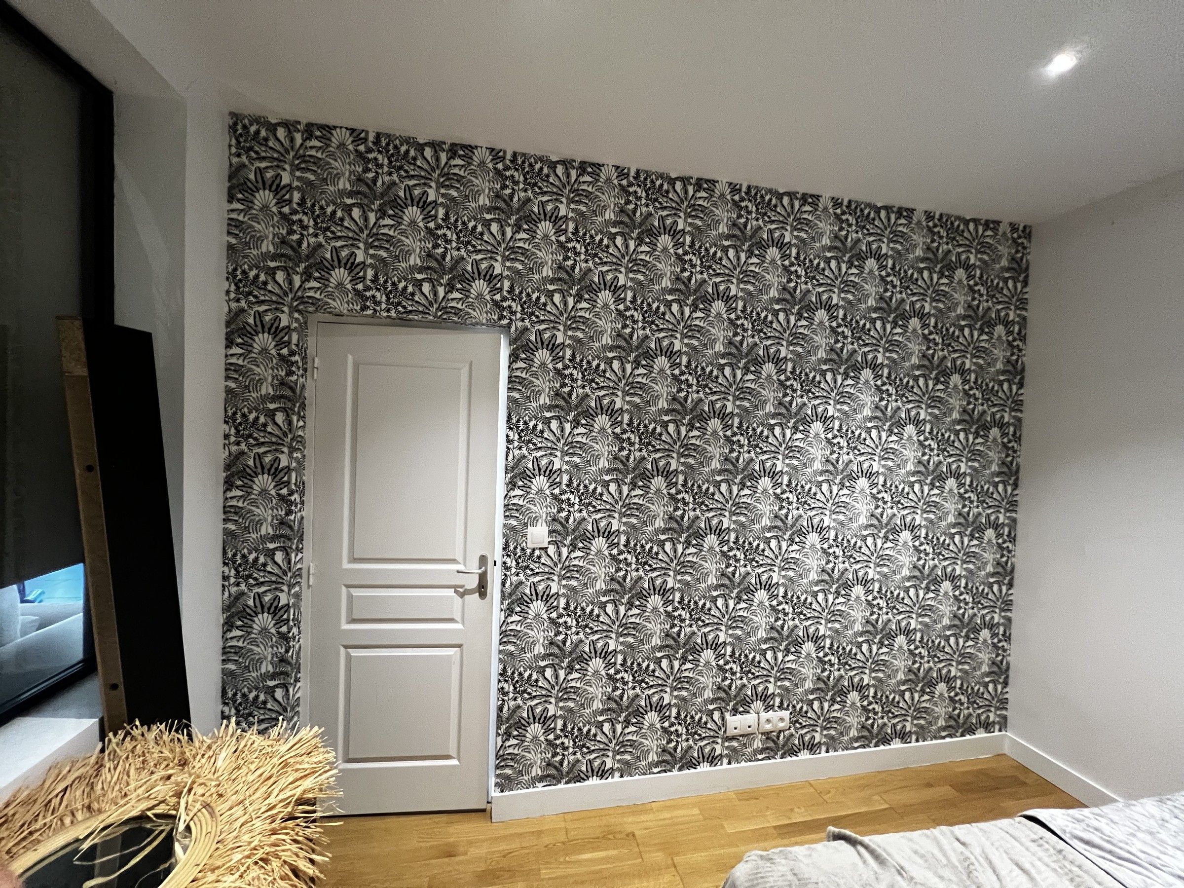 Mur en papier peint à motif de feuillage gris, à côté d’une porte moulurée blanche