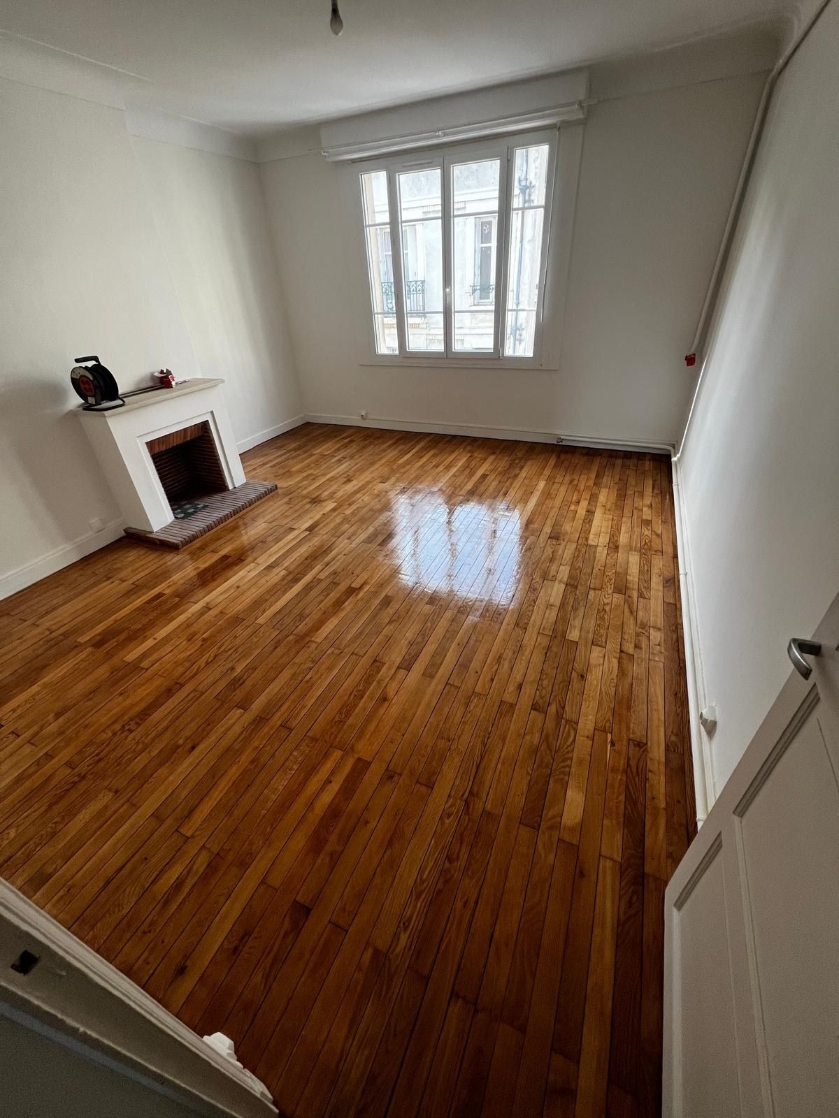 Pièce vide au parquet en bois massif fraîchement verni, avec une cheminée et une fenêtre