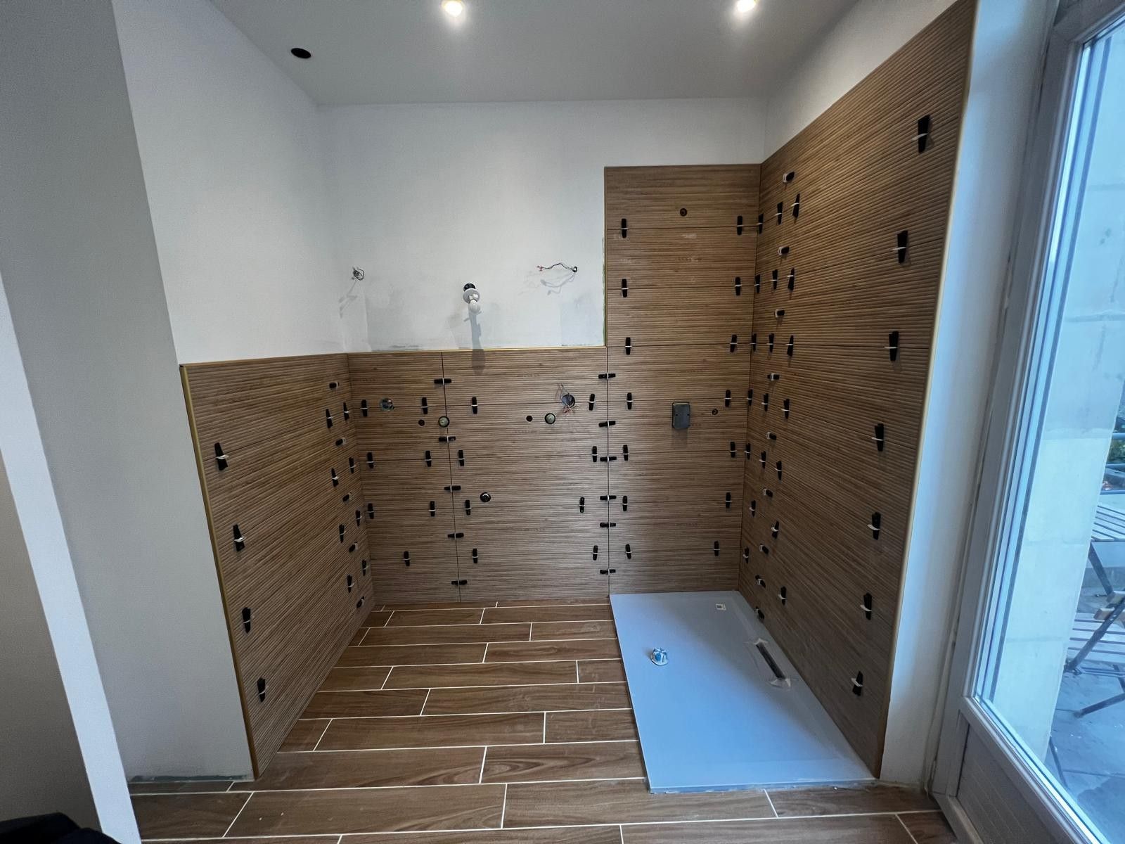 Salle de bain en cours de carrelage : faïence et sol aspect bois, receveur de douche extra-plat