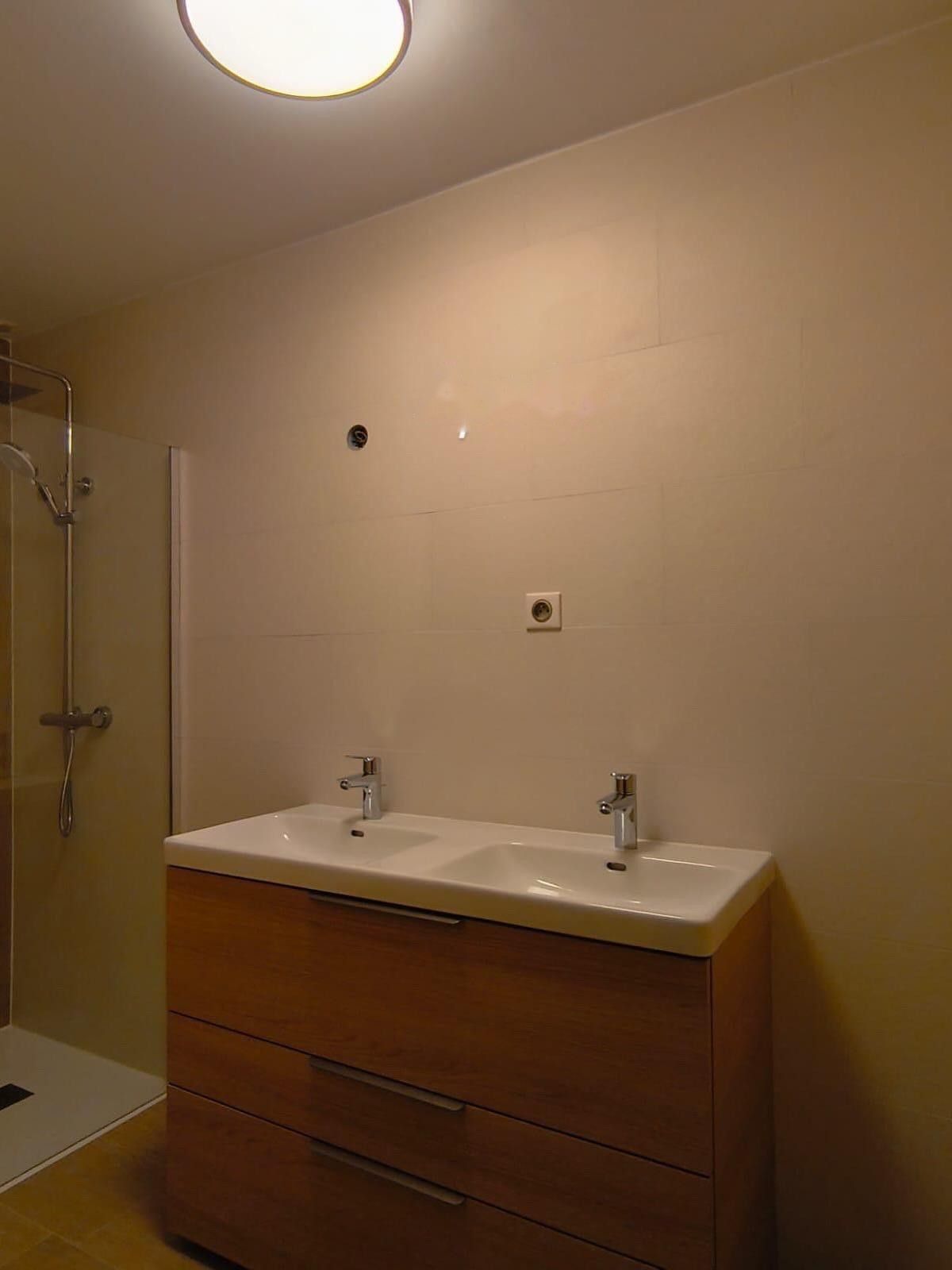 Après travaux : meuble deux vasques en bois sur un mur carrelé beige, au même emplacement