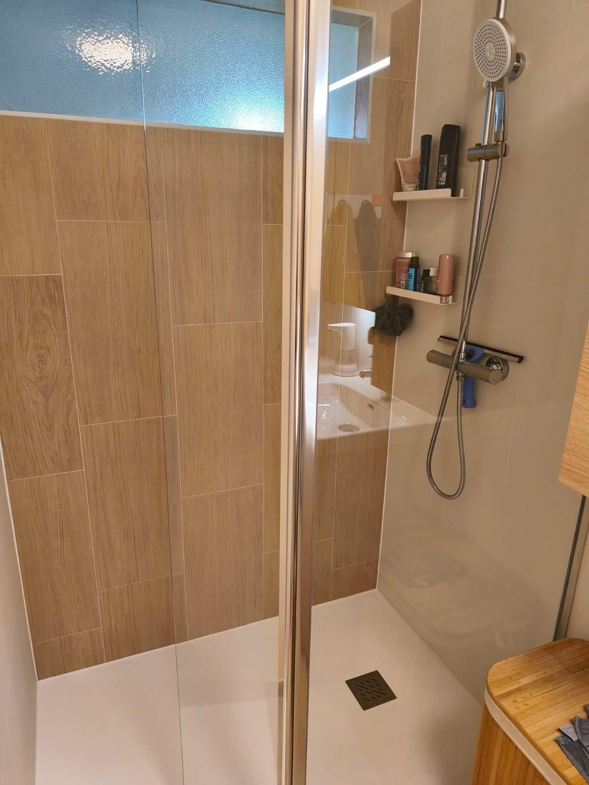 Douche équipée d’une colonne de douche, habillée de faïence aspect bois jusqu’au plafond