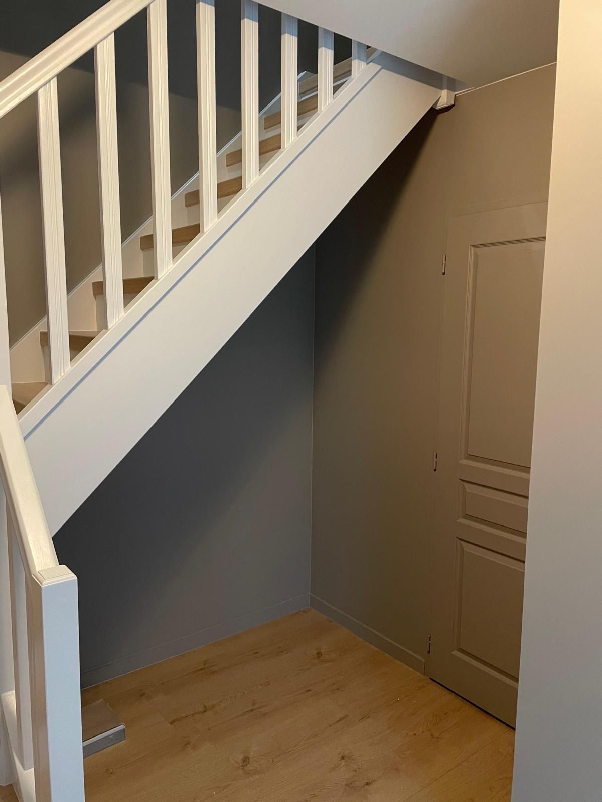 Dessous d’escalier fermé par une porte, avec un sol en lames de bois clair